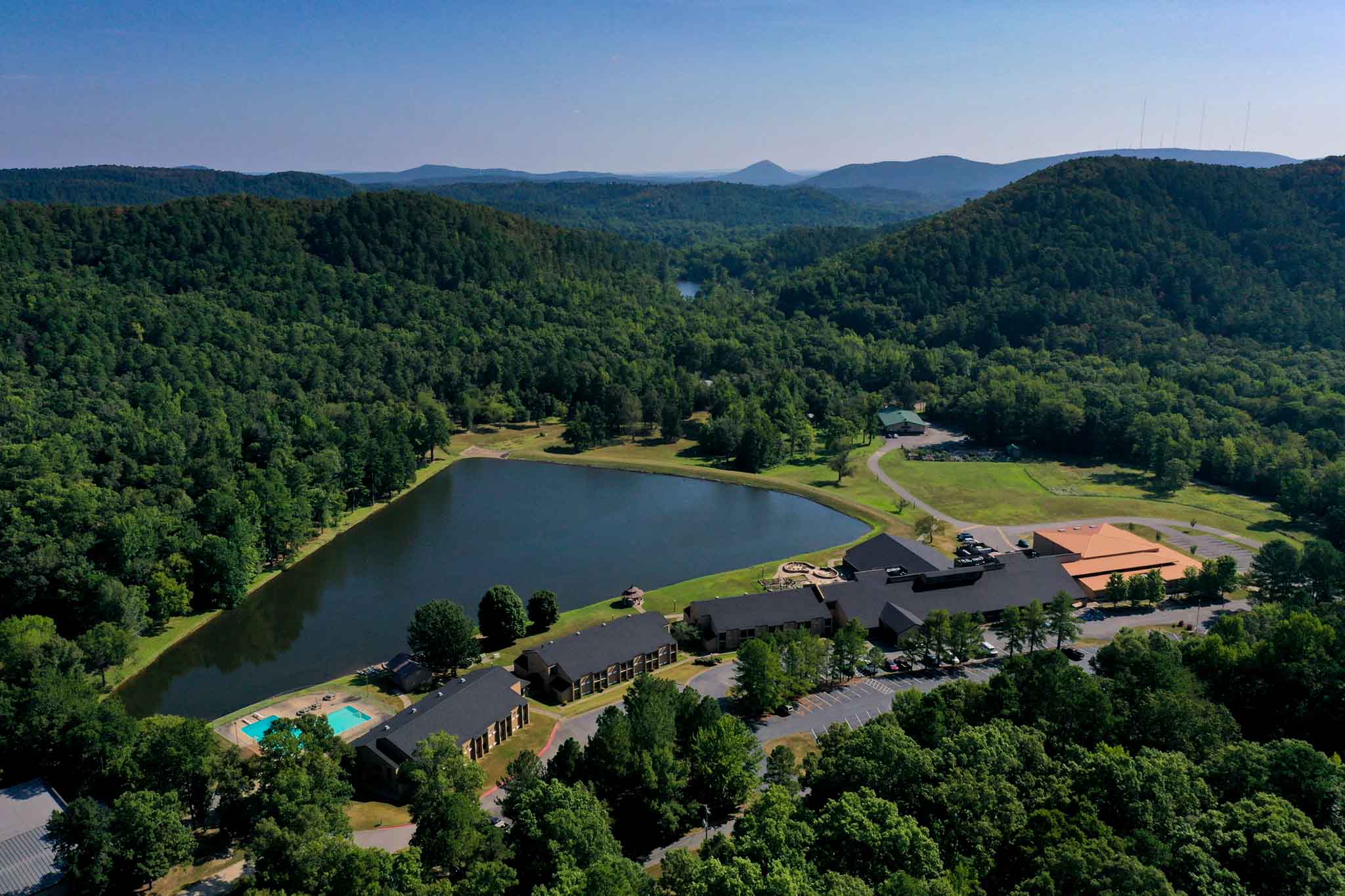 Aerial view of The Vines Center: several buildings on the edge of a pond in the mountains.